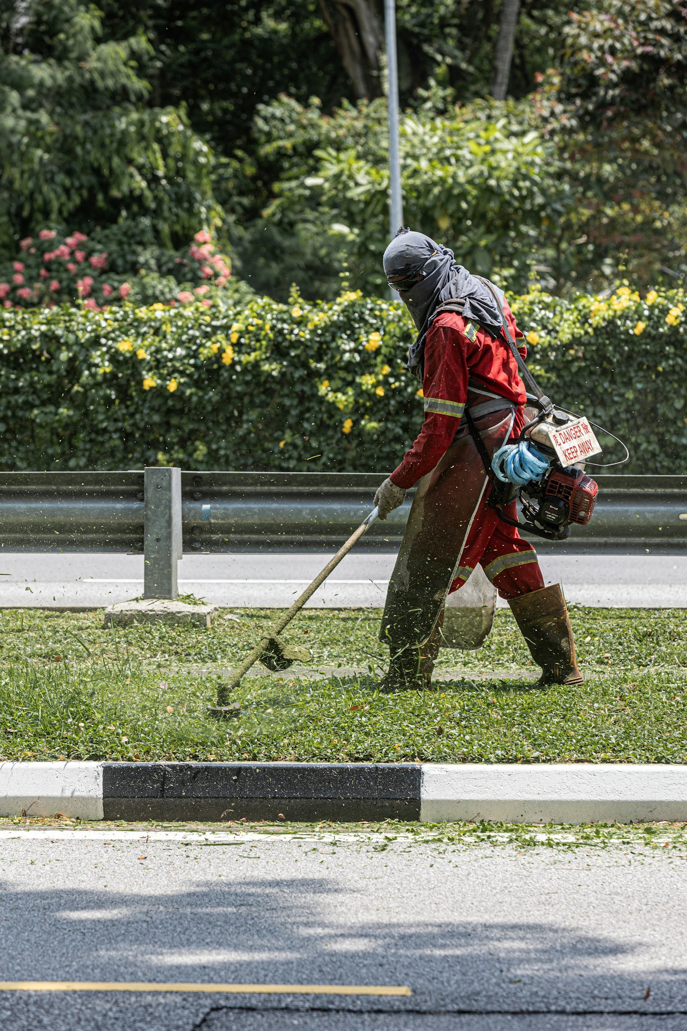 Opérateur casqué débroussaillant une bordure en herbe haute